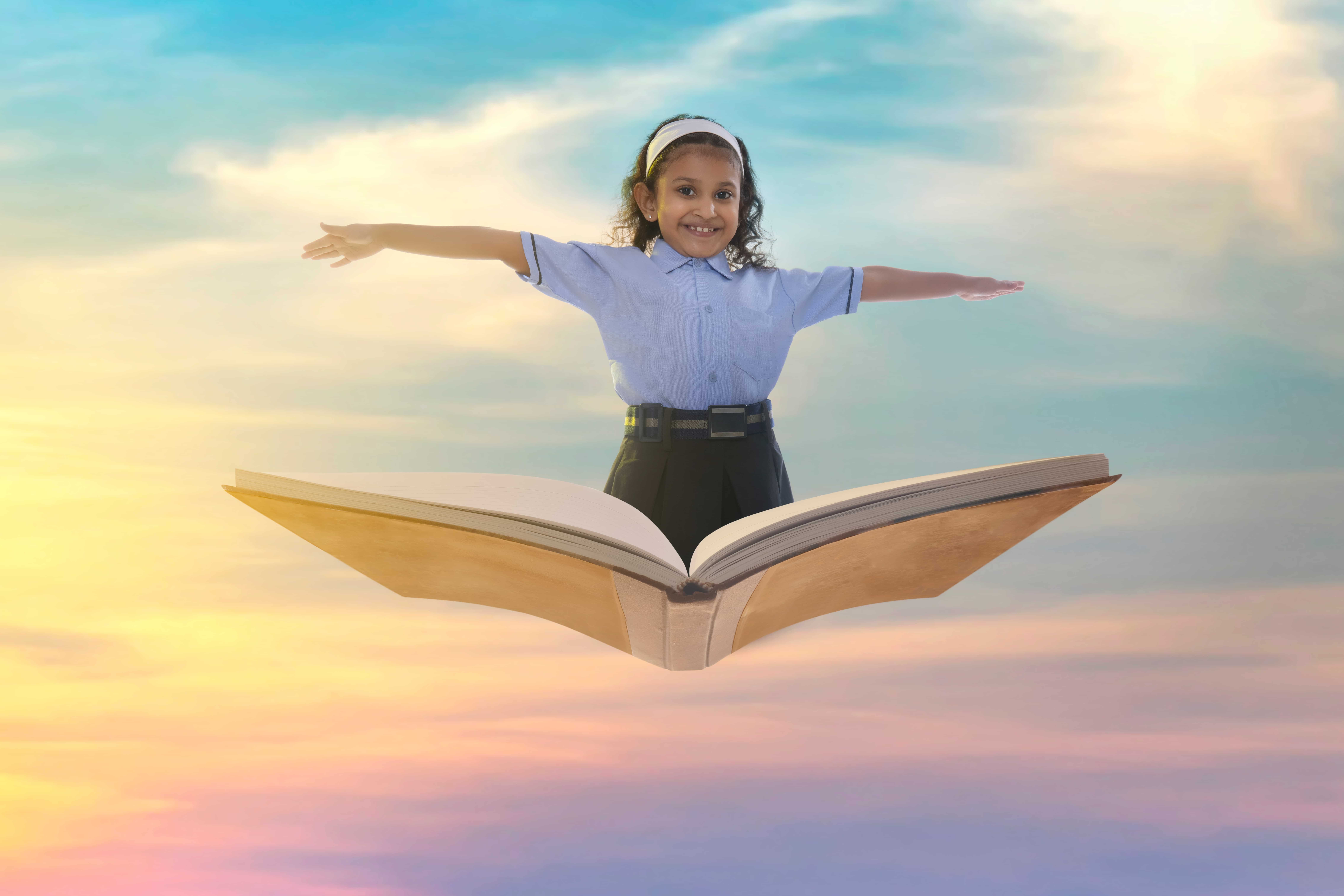 Happy student in school uniform standing on an open book against the sky, representing knowledge and growth